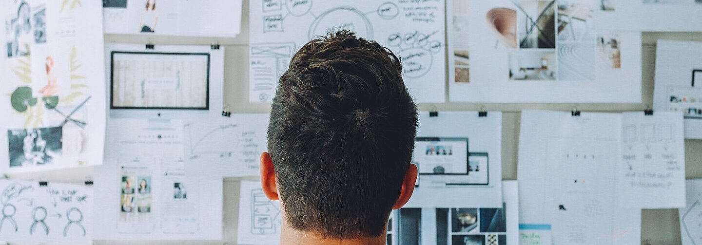 Ein junger Mann steht vor einer Wand mit vielen Zetteln und liest diese.