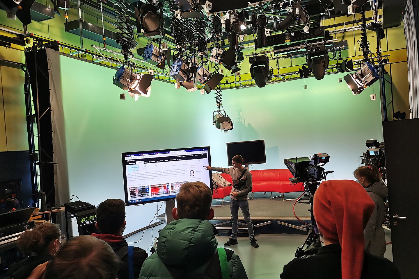 HTWK-Angehöriger präsentiert das Medienlabor mit Greenscreen einer Schulgruppe