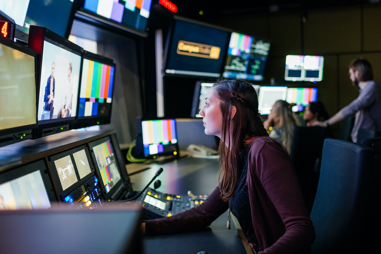 Studierende sitzt im HTWK-TV-Studio vor vielen Bildschirmen neben- und übereinander.